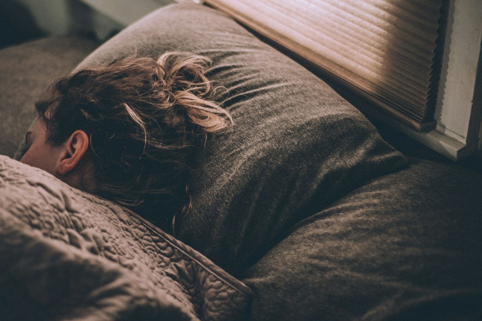 A woman asleep on a pillow by a window with the blinds down